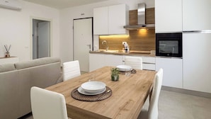 A modern kitchen with white cabinetry, a wooden dining table, and a built-in oven.
