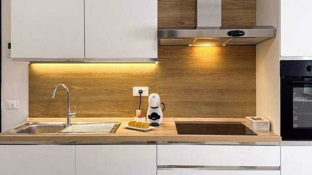 A modern kitchen with a stainless steel sink, wooden backsplash, and a built-in oven.