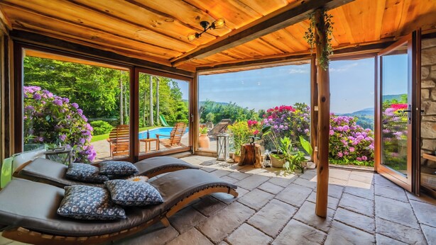 A covered outdoor seating area with lounge chairs and a stone floor, overlooking a pool and lush garden. - Trakoscan Castle View Pool House /w Private Spa (Bednja)