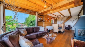 A cozy cabin interior with a leather sofa, a glass coffee table, a wooden ceiling, and a wood-burning stove. - Trakoscan Castle View Pool House /w Private Spa (Bednja)