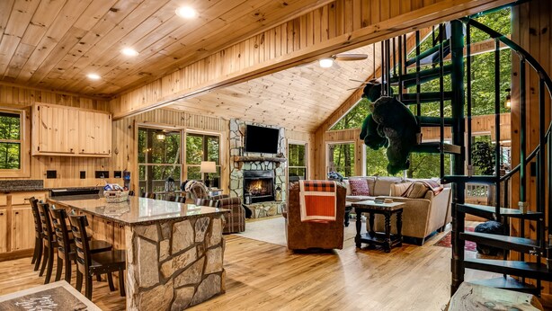 Un intérieur de chalet en bois spacieux, doté d’une cheminée en pierre, d’un coin repas et d’un salon confortable.
