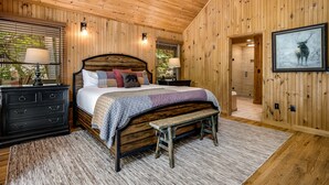 Une chambre à coucher aux murs lambrissés, avec un lit, des tables de chevet, un banc et un tableau encadré accroché au mur.