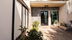 A building entrance with a stone facade, a glass door, and potted plants.