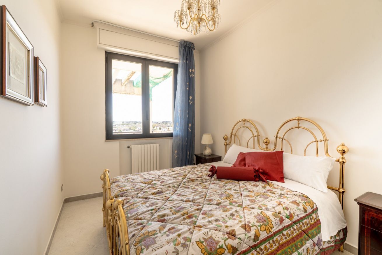 Una camera da letto con un letto, una finestra con tende, un lampadario e un termosifone.