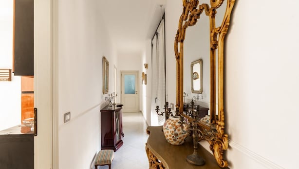A hallway with a large ornate mirror, a wooden console table with a vase, and a small bench.