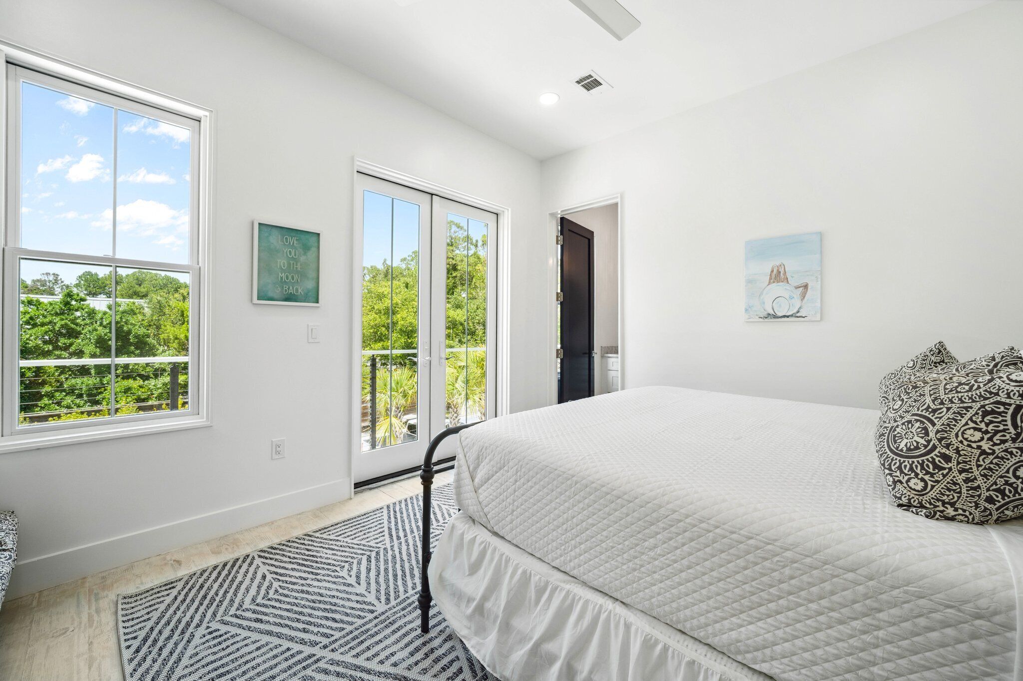 A bedroom with a large bed, a view of greenery through the window, and a door leading to a balcony.