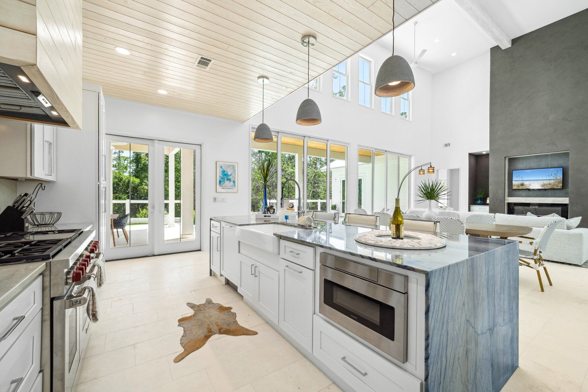 A modern kitchen with white cabinetry, a marble island, and a large window overlooking a garden.