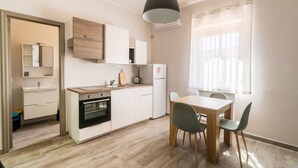 A modern kitchen with white cabinets, a wooden countertop, and a dining area with a table and chairs. - GuestHost - Lovely Apartment in Barletta (Barletta)