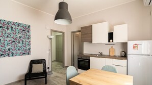 A compact kitchen with a dining area, a black chair, a wooden table, and a hanging pendant light. - GuestHost - Lovely Apartment in Barletta (Barletta)
