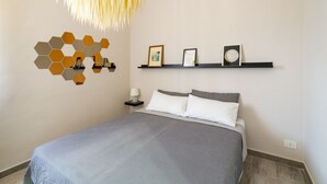 A modern bedroom with a bed, a wall-mounted hexagonal light fixture, and a shelf with framed pictures. - GuestHost - Lovely Apartment in Barletta (Barletta)