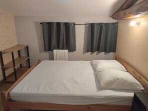 Ein Einzelbett mit weißer Bettwäsche, einem Holz-Kopfstück, einem Regal und einem Heizkörper.