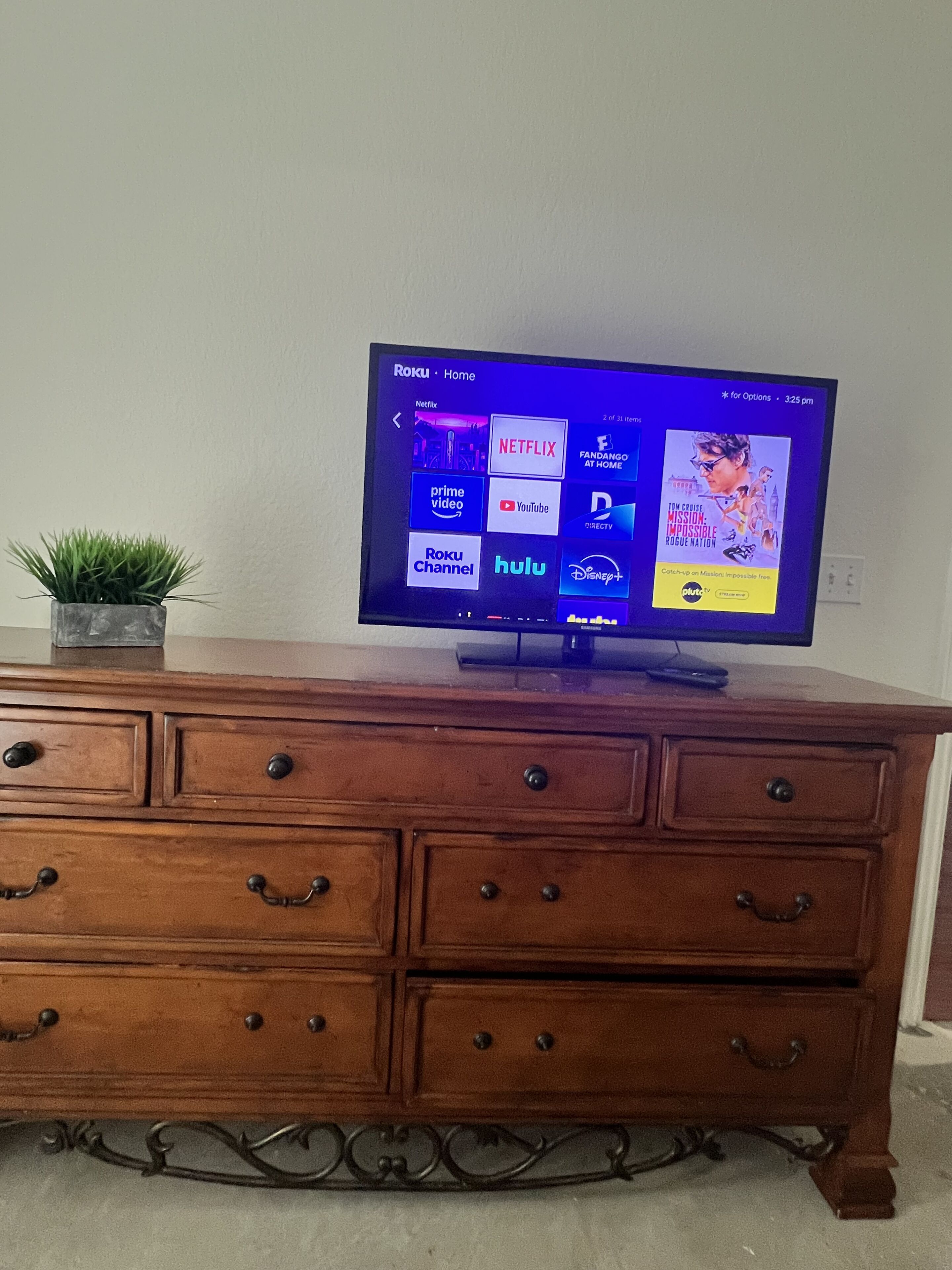 A flat-screen TV on a wooden dresser with drawers, displaying a Roku interface with various streaming services.