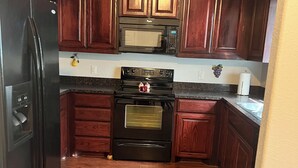 Una cocina con armarios de madera, un refrigerador negro, un microondas, una estufa y un lavamanos.