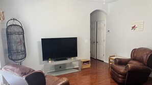 Una sala de estar con una televisión de pantalla plana, dos sillones de cuero, una mesita de madera y una jaula decorativa.