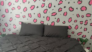 Un dormitorio con una cama, dos almohadas y una pared con estampado rosa y negro.