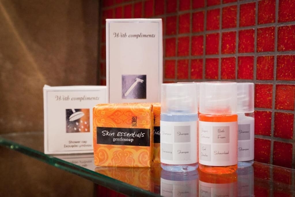 A bathroom shelf with toiletries including a box labeled "Skin Essentials gentlesoap," a bottle of shampoo, and a bottle of bath foam.
