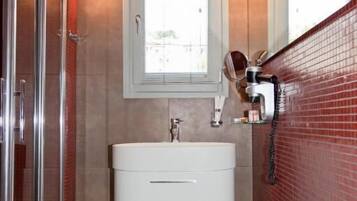 Un baño moderno con cabina de ducha de vidrio, tocador blanco y paredes con azulejos rojos.
