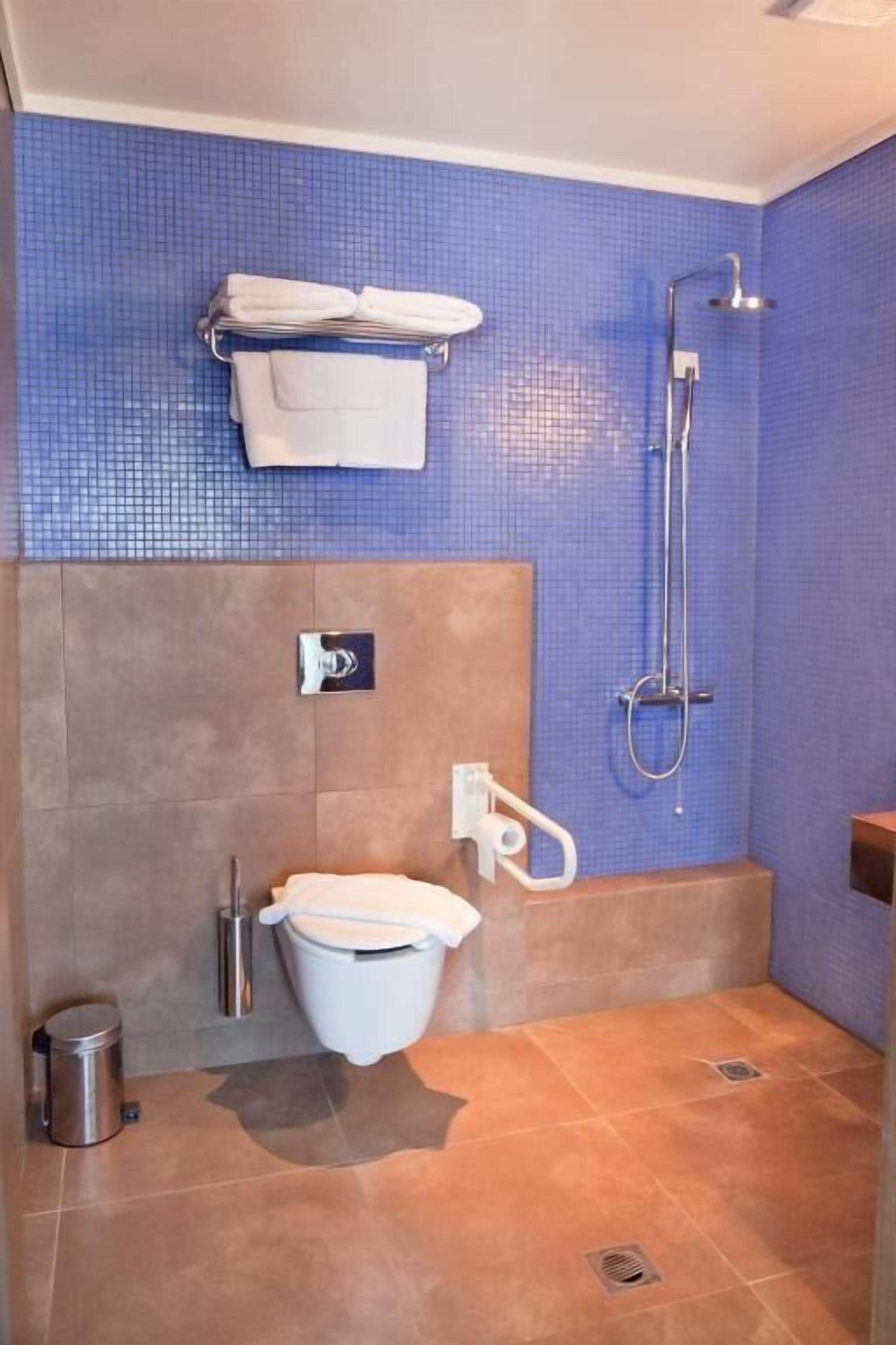 Un baño con pared azul de azulejos, un inodoro blanco, una ducha y un perchero para toallas.