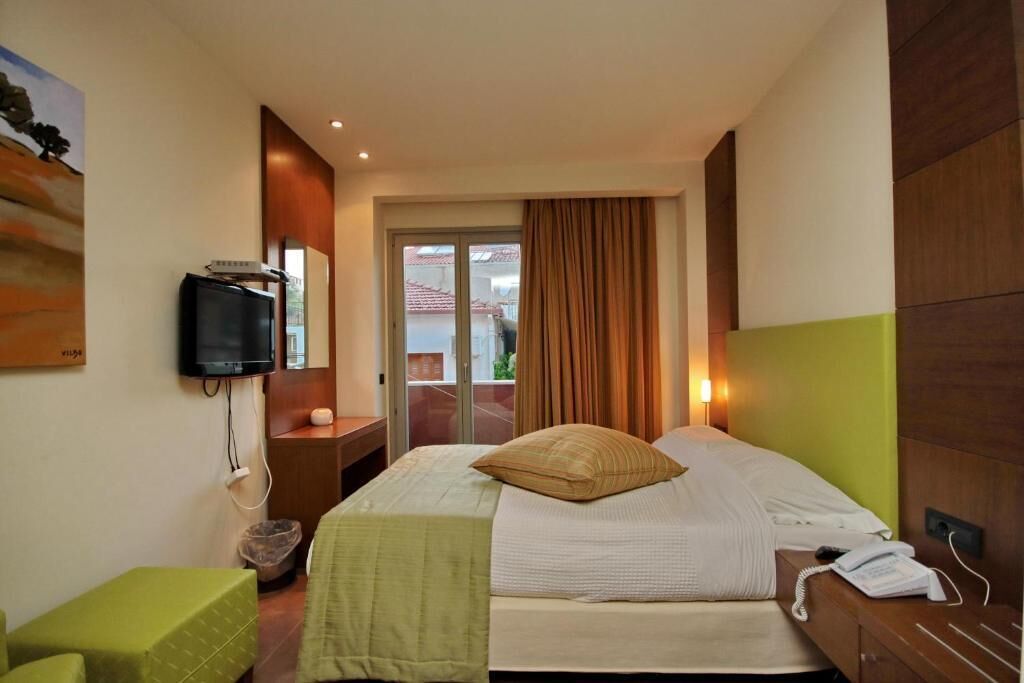 A hotel room with a bed, a television on the wall, a telephone, and a view of the outside through a glass door.