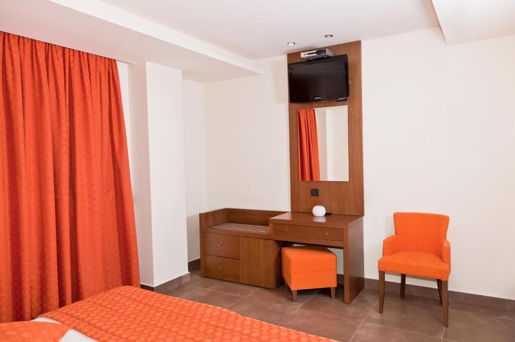 Una habitación de hotel con una cama, un escritorio de madera, una silla y un televisor colocado en la pared.
