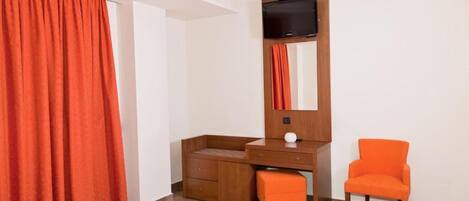 Una habitación de hotel con una cama, un escritorio de madera, una silla y un televisor colocado en la pared.
