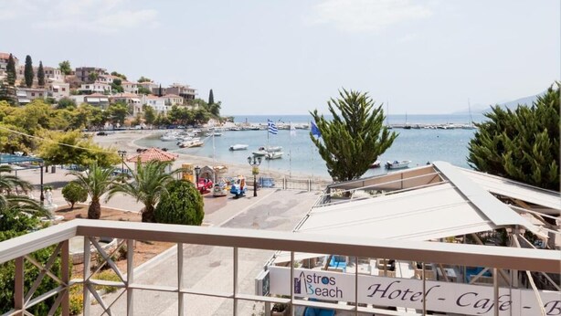 A coastal view from a balcony overlooking a marina with boats, a beach, and buildings in the background.
