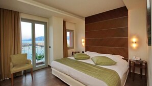 A hotel room with a bed, a chair, a nightstand, and a view of the sea through a sliding door.