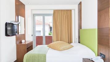 A hotel room with a bed, a television on a stand, a bedside table with a phone, and a view of the outside through a glass door.