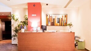 A reception desk with a red accent wall, a modern abstract painting, and potted plants.