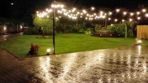 Un'area esterna illuminata da luci a stringa, con pavimento bagnato e prato.