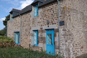 A stone building with blue windows and doors, a sign indicating a historical site, and a small garden area in front. - Country house (Saint-Rémy-du-Plain)