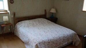 A bedroom with a wooden bed, a bedside table with a lamp, and a patterned wallpaper.