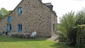 A stone building with a sloped roof and a small patio area with metal chairs and a table.