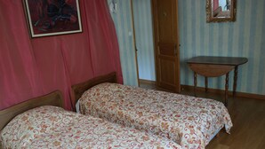 A bedroom with two beds, a wooden table, and a door leading to another room.