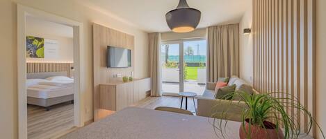Una habitación de hotel moderna con una cama, zona de comedor, televisor y vistas al exterior.