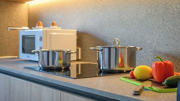 A kitchen with a microwave, two stainless steel pots, a cutting board with vegetables, and a knife.