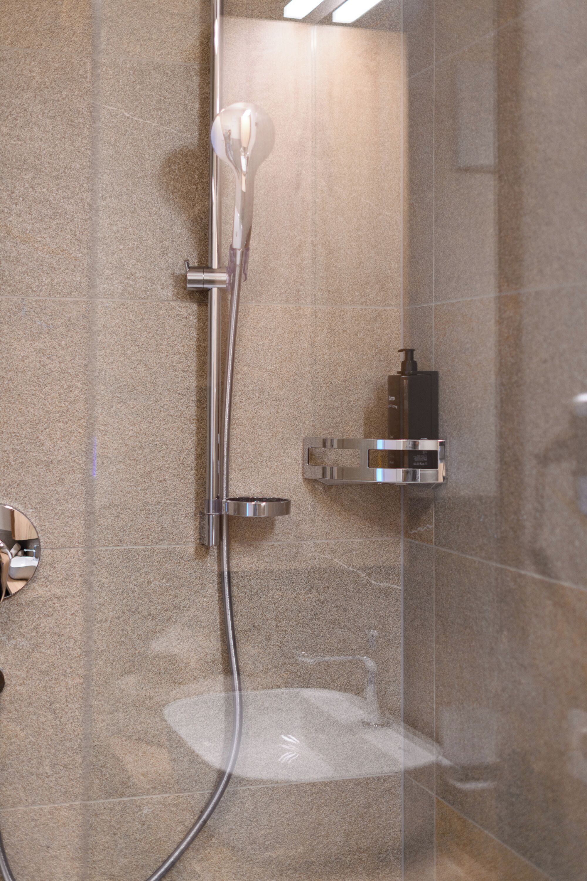 A modern shower with a handheld showerhead, a wall-mounted soap dispenser, and a chrome faucet.