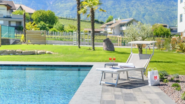 A swimming pool with lounge chairs and a bag, surrounded by a well-maintained lawn and mountains in the background.