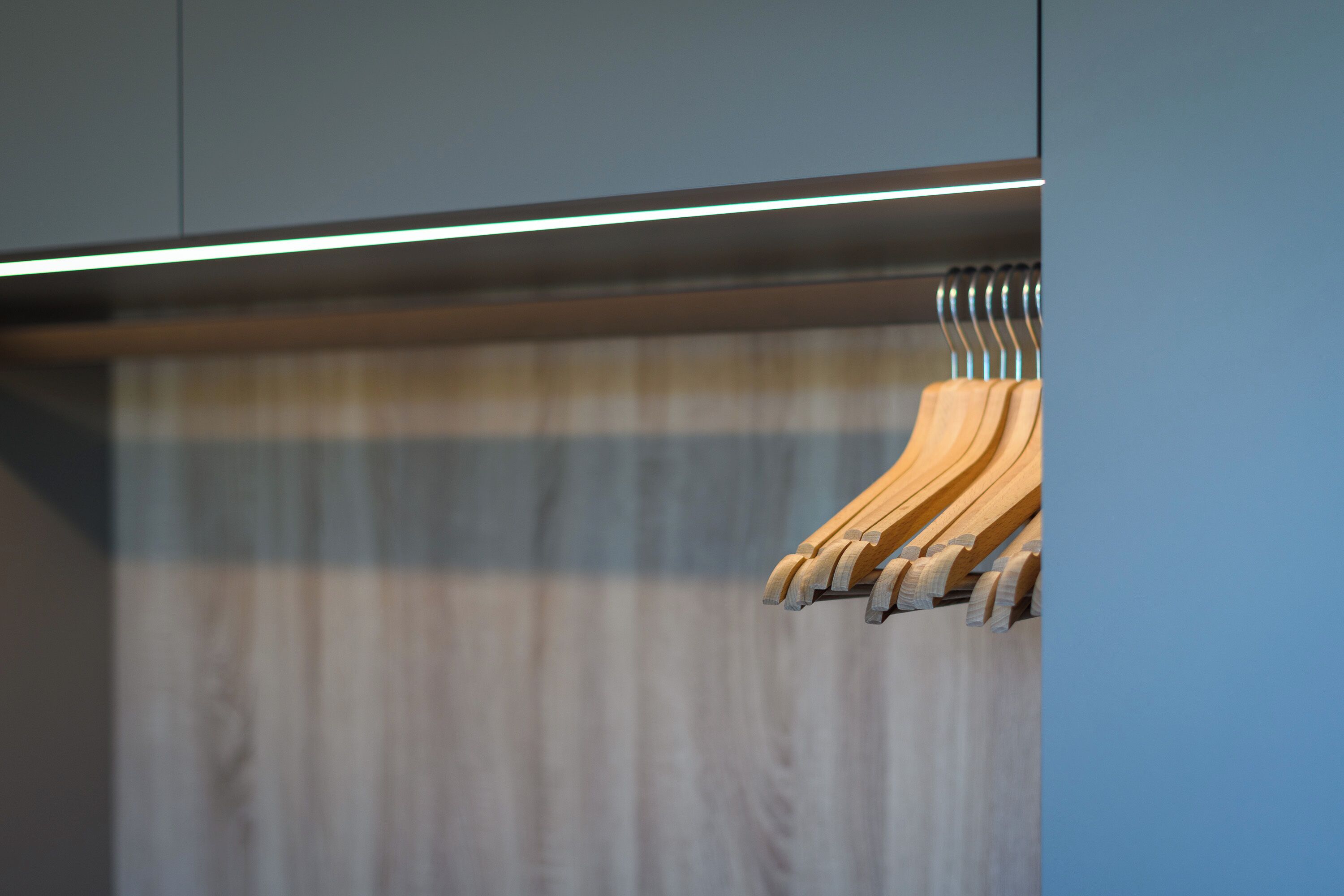 Ein Kleiderständer aus Holz an einer Wand, darüber eine horizontale Lichtleiste.
