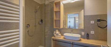 Un baño moderno con cabina de ducha de vidrio, un lavamanos blanco y un mueble de tocador de madera.