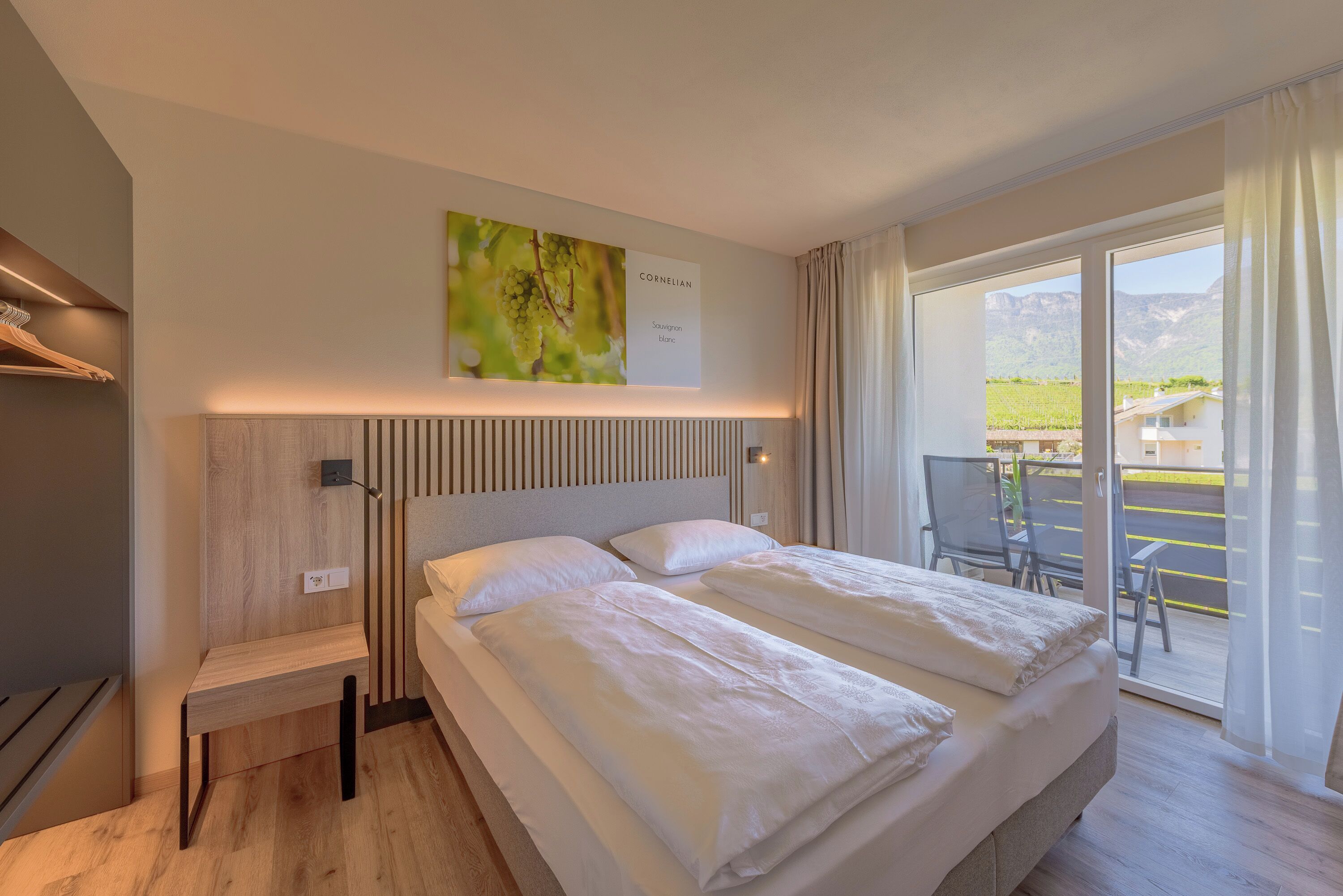 A hotel room with a bed, a headboard, a small table, a wall-mounted artwork, and a view of the outdoors through a sliding door.