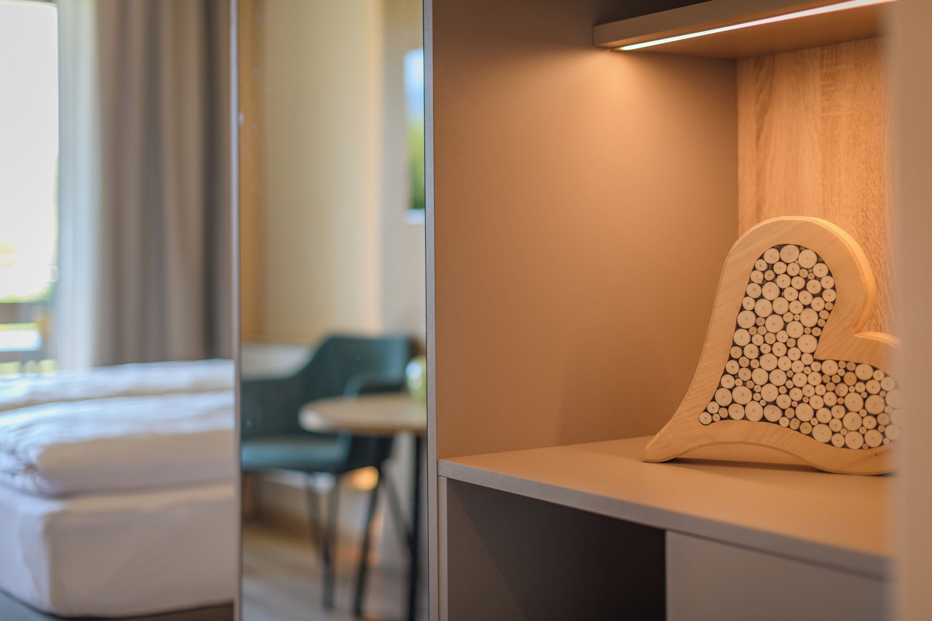 Een hotelkamer met een bed, een stoel en een decoratief houten object op een plank.
