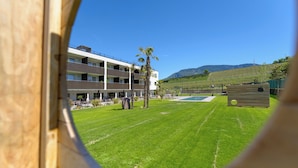 A view through a window of a building with a grassy lawn, palm trees, and a pool.