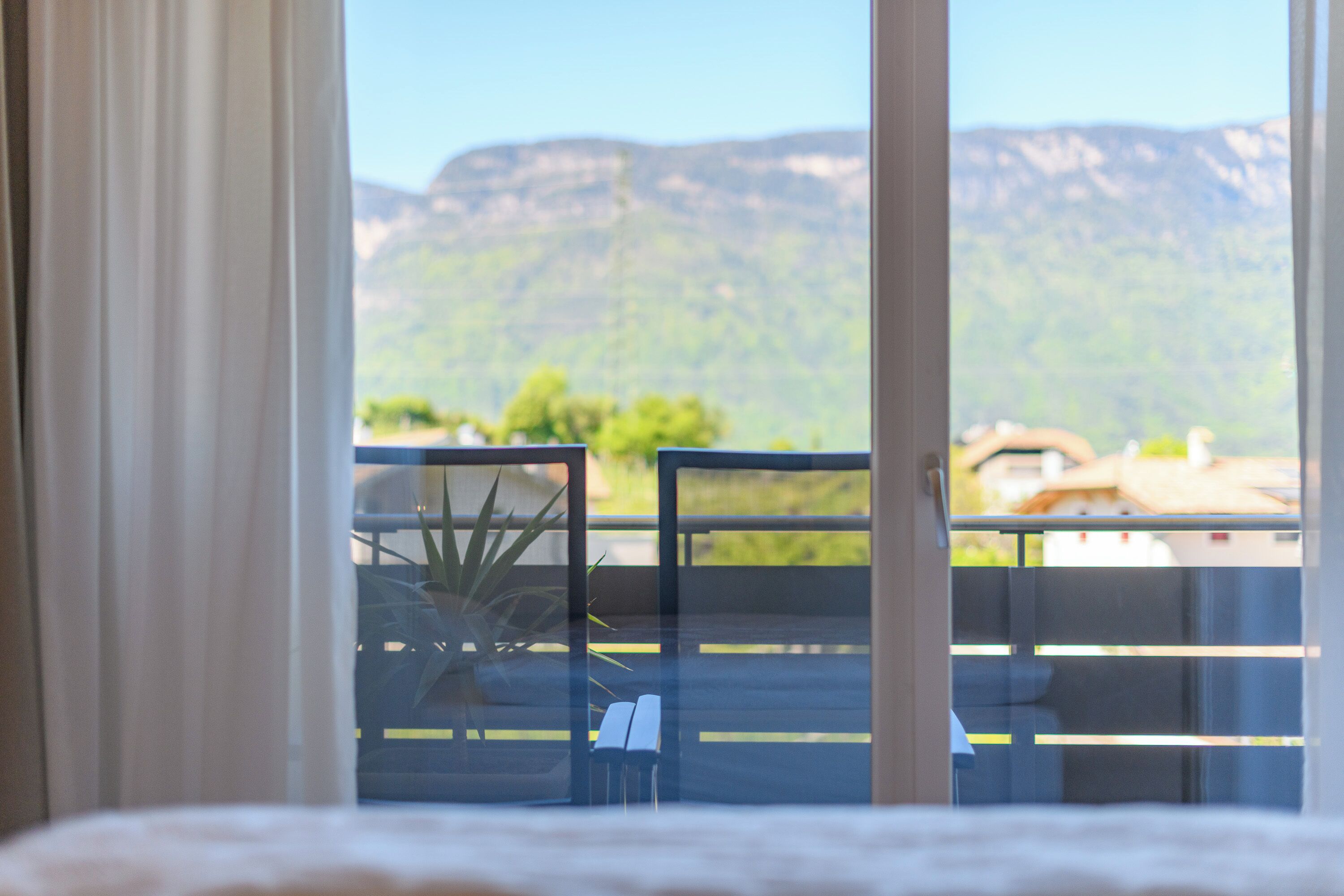 A balcony with a view of mountains, a potted plant, and a chair.