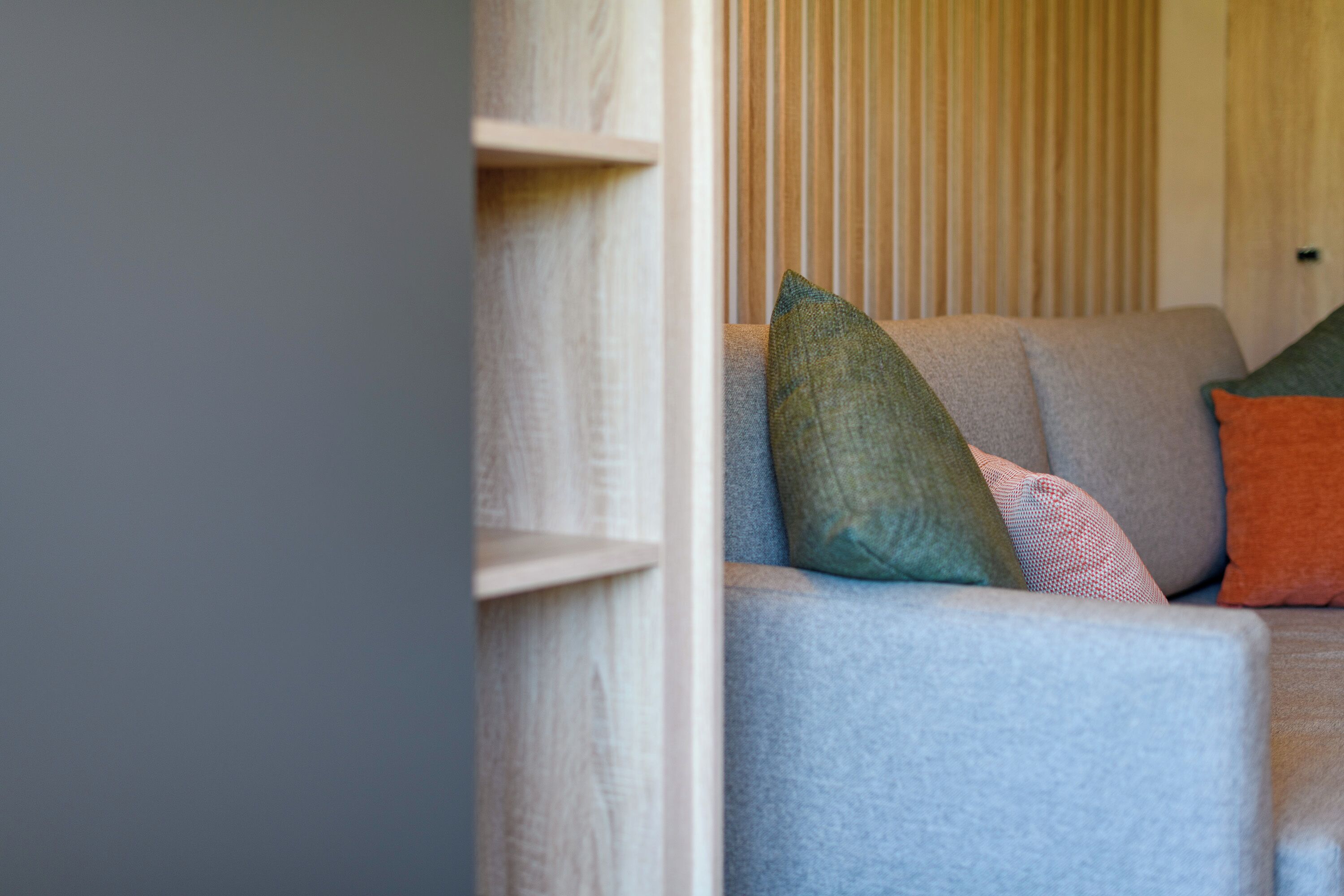 Una habitación con un sofá gris, una estantería de madera y un panel de madera vertical.
