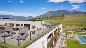 A modern hotel with rooftop seating, a swimming pool, and a view of mountains.
