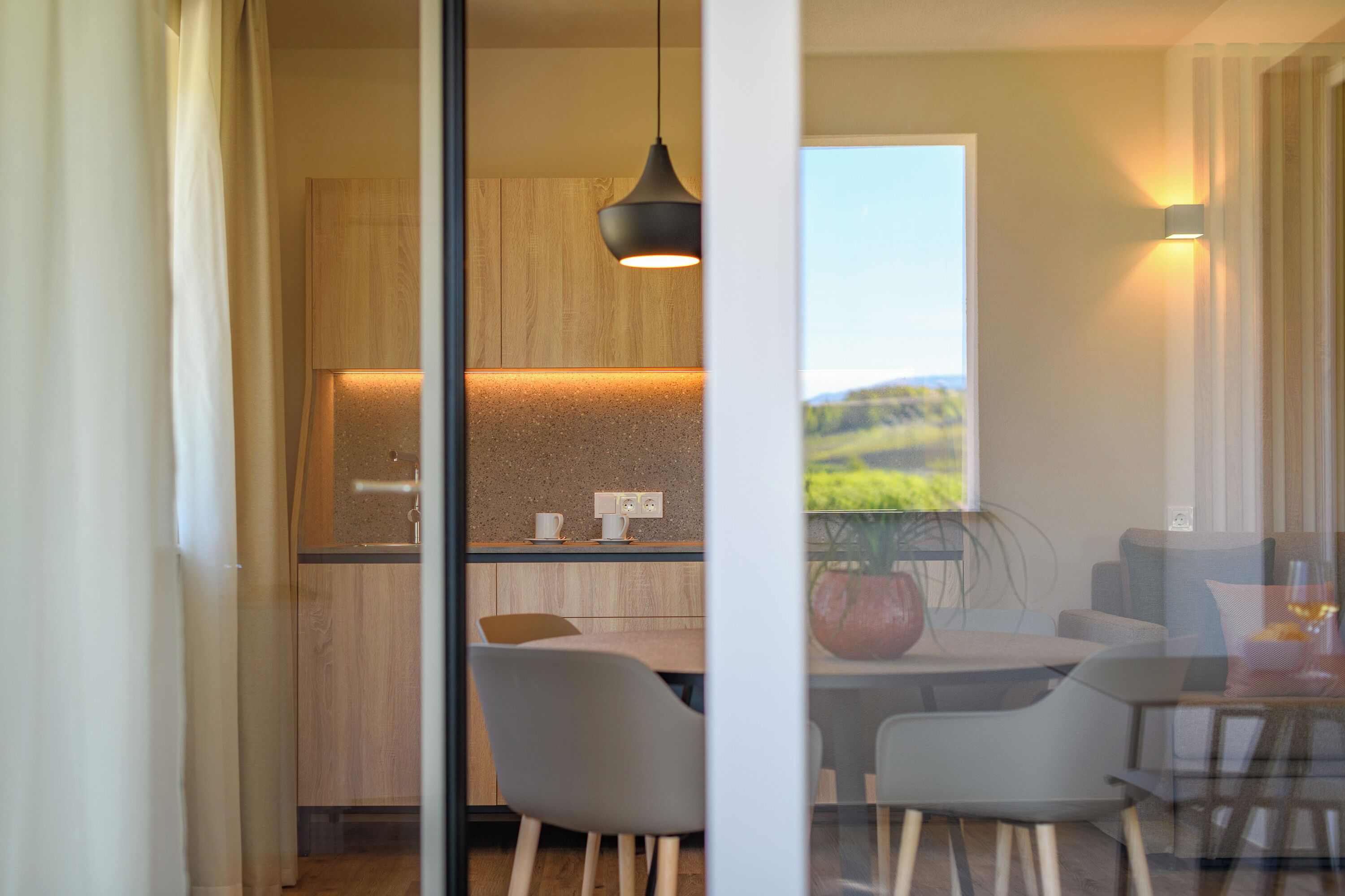 Eine moderne Küche mit Holzschränken, einer hängenden Pendelleuchte und einem Essbereich mit Tisch und Stühlen.