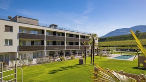 A modern hotel with multiple balconies, a swimming pool, and a well-maintained lawn.