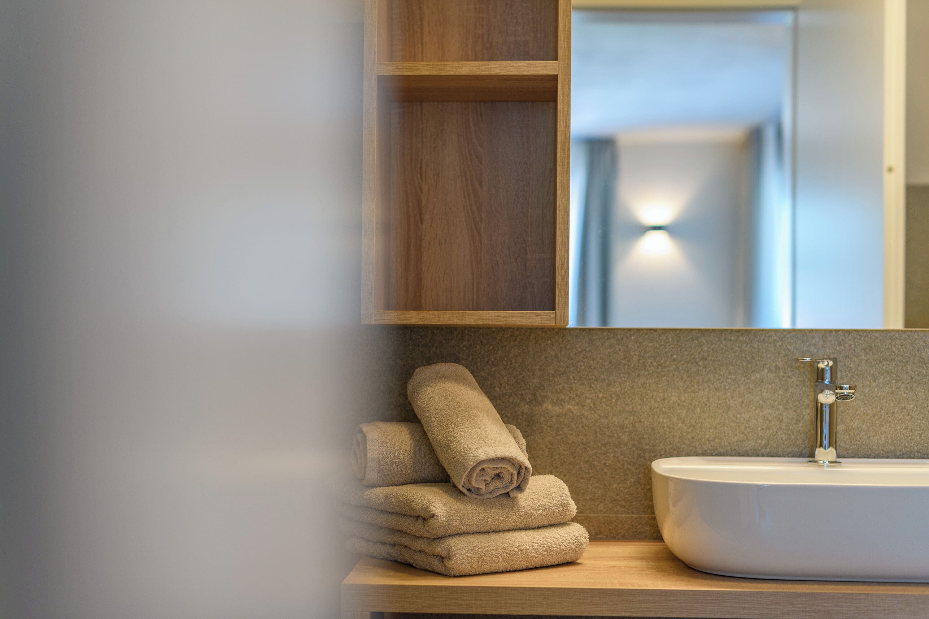 Un baño con tocador de madera, un lavabo blanco y un espejo que refleja una puerta.