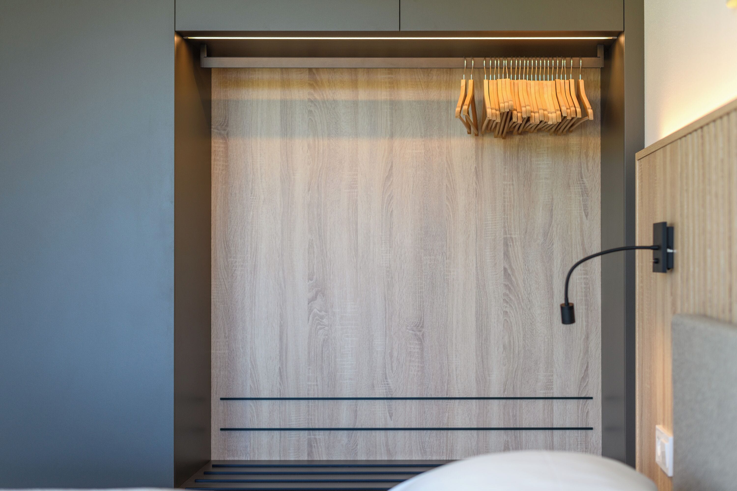 Un dormitorio moderno con un armario de madera, una percha y una cama.